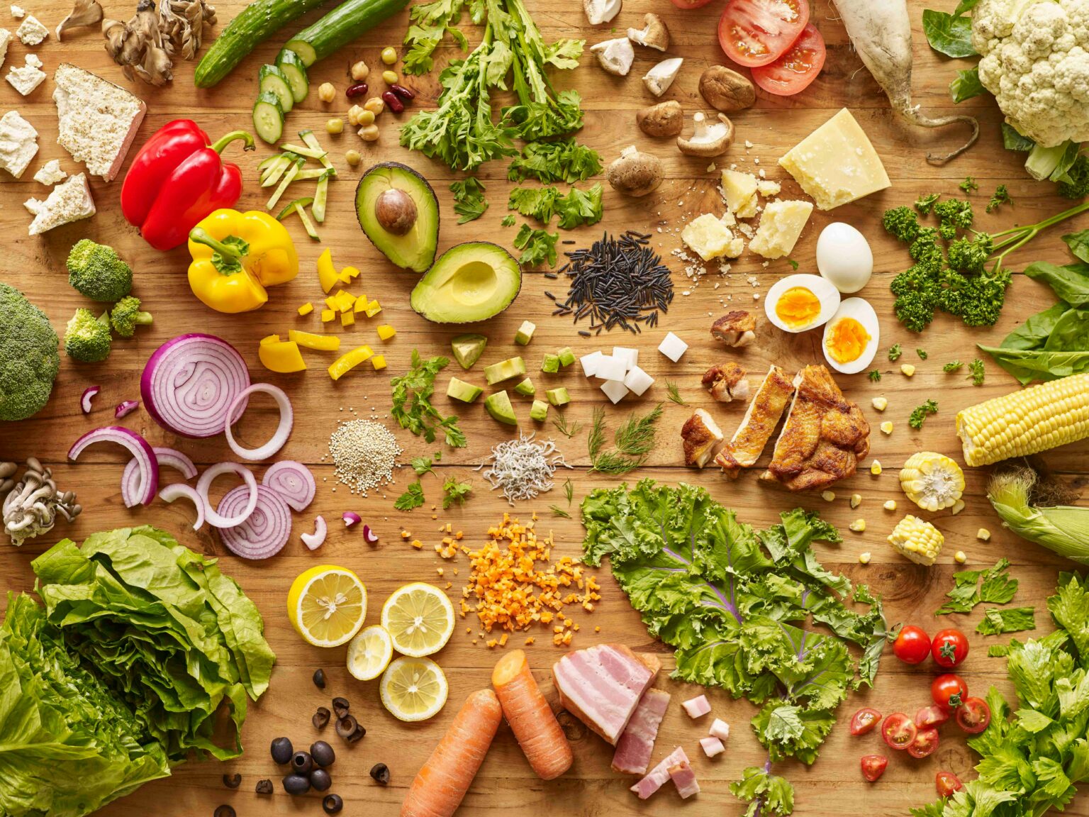 Assortiment coloré de légumes, fruits, légumineuses, céréales et protéines végétales sur une table en bois.